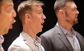 Three men shown in a profile view sing.