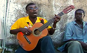 Brushy sings and plays the guitar in front of a group of men.