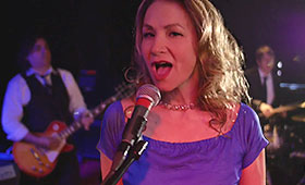 Osborne sings into a microphone while her band performs behind her in a dark room.