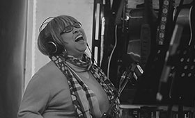 A black and white photo of Staples singing into a microphone in a recording studio.