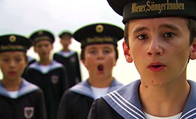 A close-up photo of a boy singing with four boys in the background.