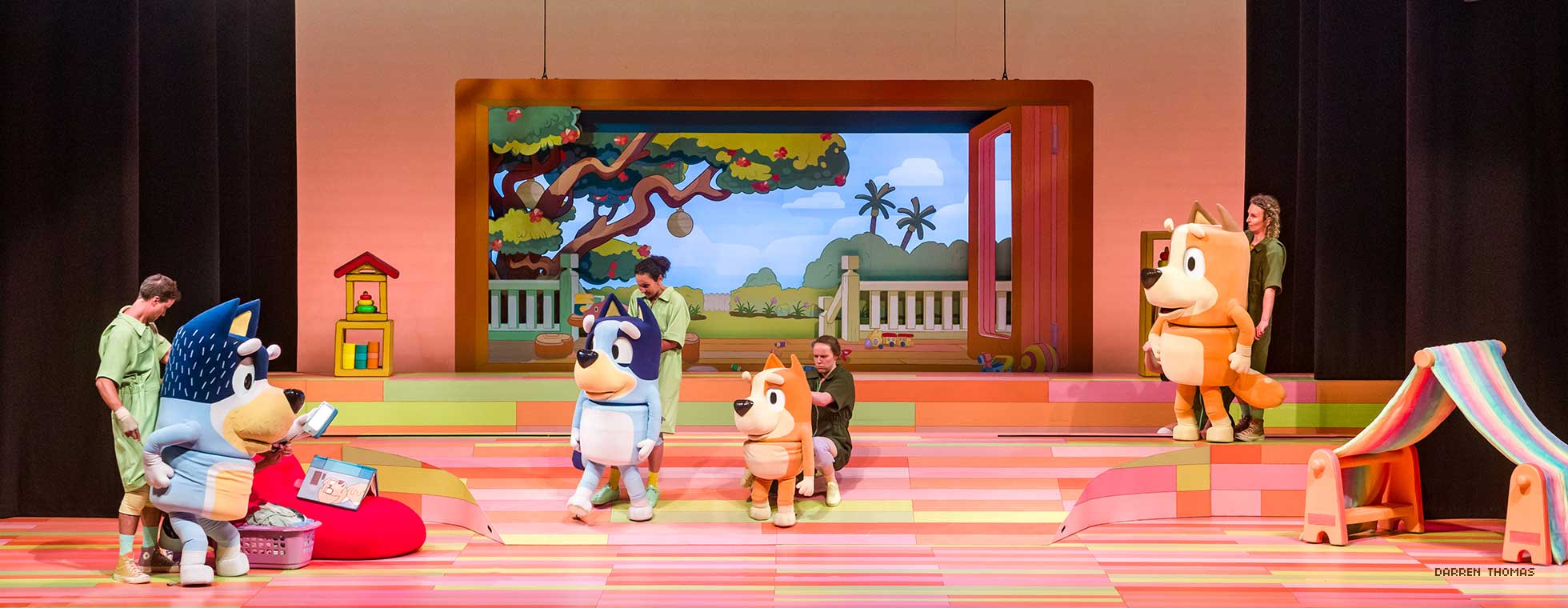 Live actors control the movements of four adult-sized dog puppets in a scene inside the family’s house. 