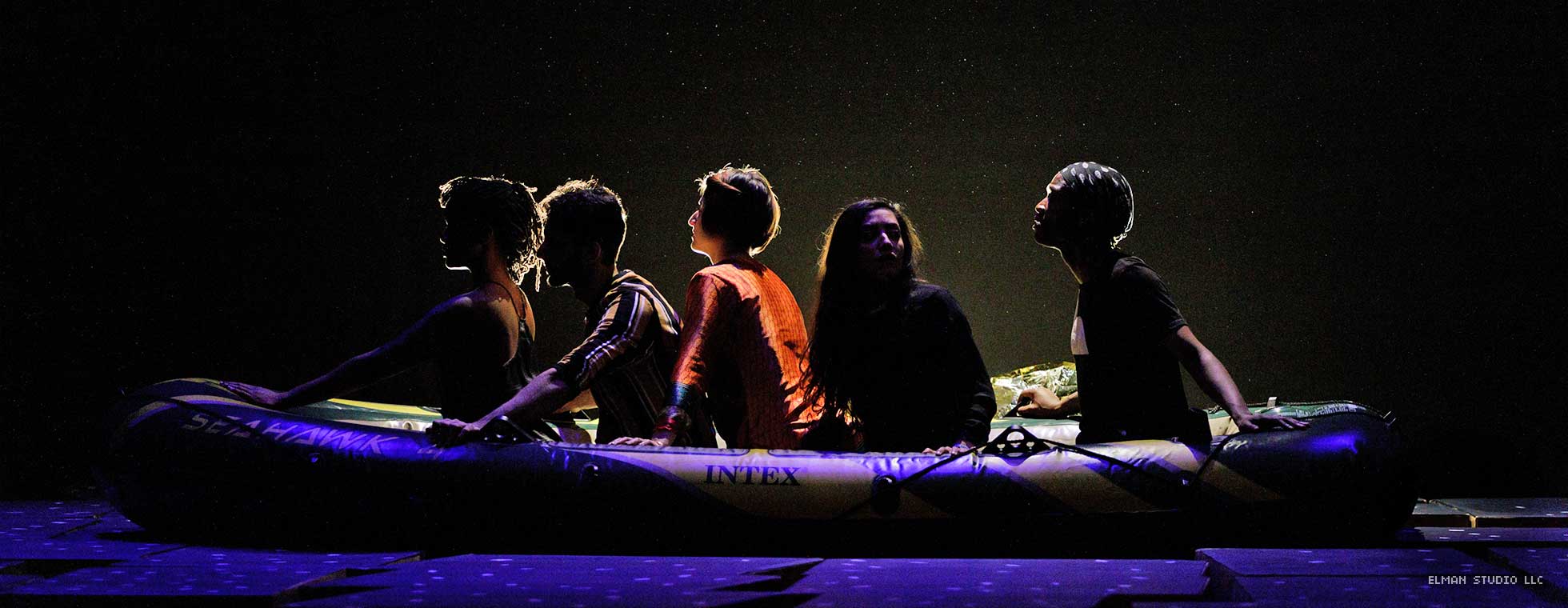 Five actors sit in an inflatable boat.