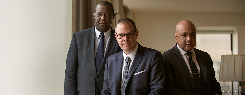 Three man in suits look directly at the camera.