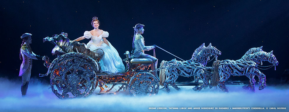 Cinderella smiles while she sits in a decoratively-lit horse-drawn carriage prop.