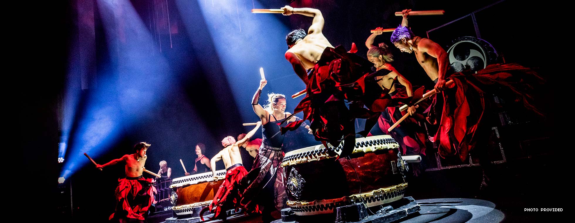 Shirtless men in flowing robes bang thick sticks on large drums.
