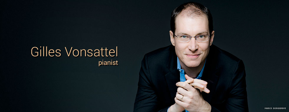 Pianist Gilles Vonsattel clasps his hands together while he looks and smiles at the camera.