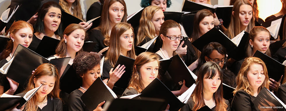 Female chorus members each hold a songbook while they sing.