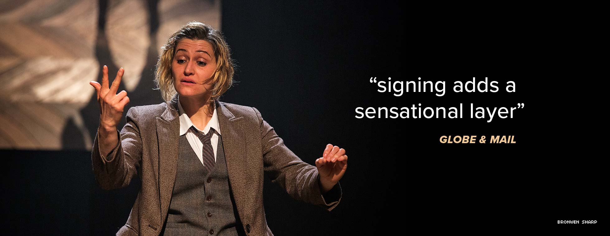 An actor looks down as she makes sign language gestures. The Globe and Mail says “signing adds a sensational layer.” 