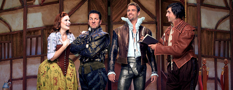 All dressed in medieval-style costumes, a female actor puts her hand to her bosom while looking at three men who make a funny face, flash a smile and read from a book.