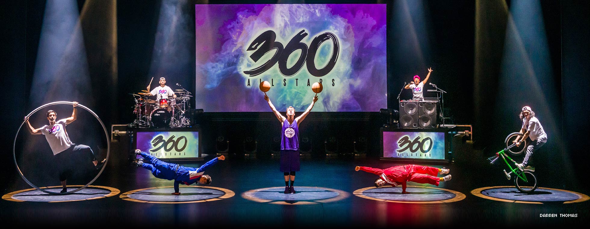 Performers on a stage breakdance, juggle, do bike stunts, and play music.