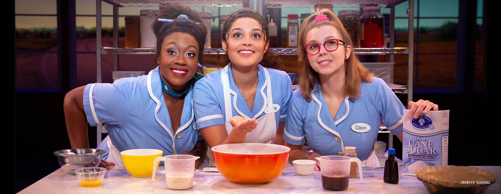 Three diverse women stand at a counter surrounded by pie-baking ingredients.