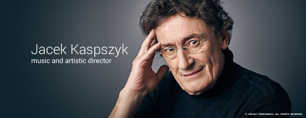 Warsaw Philharmonic Orchestra Music and Artistic Director Jacek Kaspszyk holds his hand to his forehead and looks at the camera in an official portrait.