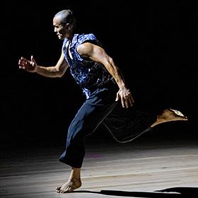 A dancer is shown in a running man pose — with one foot on the ground and the other behind, and one arm reaching forward.