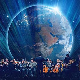 An orchestra sits on a stage below an overhead projection of an image of Earth from space. 