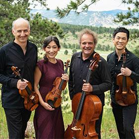 Four smiling musicians stand in a row and hold their string instruments.