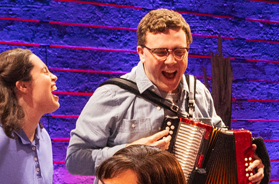 A woman happily sings on the left as she looks at a man to the right who plays the accordion.