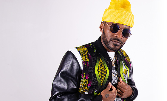 A man wearing sunglasses and boldly patterned clothes adjust his jacket.