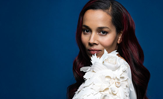 Rhiannon Giddens looks into the camera wearing a dress covered in 3 dimensional flowers.