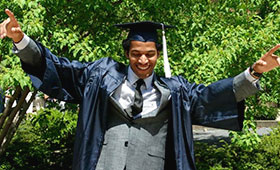 Thompson holds his hands in the air wearing his graduation cap and gown.