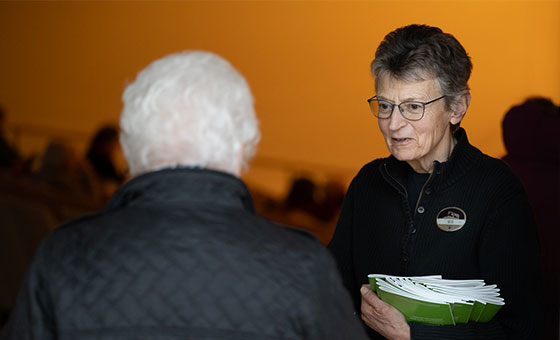 A volunteer usher hands a program book to a patron entering the auditorium.