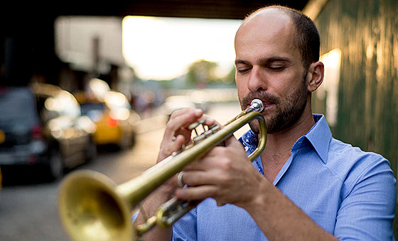 A balding man looks at his trumpet while he plays.