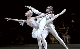 A ballerina reaches forward on one leg while a man supports her.