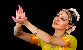 Ramaswamy holds her hands in the air with painted finger tips and wearing traditional Indian clothing and headdress.