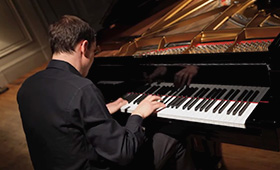 A man is seen from behind sitting and playing the piano.