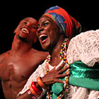 A shirtless male dancer and a female dancer dressed in traditional dress perform with Balé Folclórico da Bahia.
