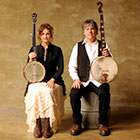The husband-and-wife musicians hold their banjos upright while they sit closely side by side.