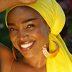 A woman wearing a brightly colored headscarf and large, round earrings, smiles for the camera.