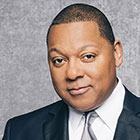 Marsalis, wearing a shirt, vest, and tie, looks into the camera.