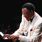 Jazz musician Ramsey Lewis plays the piano in a tuxedo.