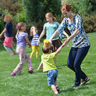 A woman and her son dance in a field of grass surrounded by other dancing children.