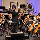 A conductor stands on a pedestal in front of the orchestra.