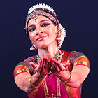 Aparna Ramaswamy cups her hands in the style of a classical Indian dance gesture while wearing a brightly colored traditional clothing.