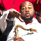 Erion Williams holds his tenor saxophone and gestures to the camera.