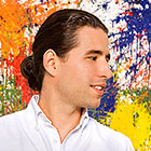 The Cuban pianist, posed in front of a splash-painted artwork, looks to the right.