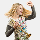 Jazz musician Bria Skonberg, with a look of excitement, holds a trumpet in her right hand and pumps her left fist in the air.
