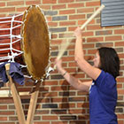 A women beats the front of a large Taiko drum.