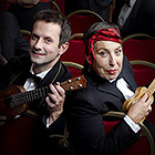 Will Grove-White and founder Kitty Lux pose with their different-sized ukuleles while sitting in chairs.