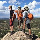 Three hikers stand at the edge of a mountain overlook.