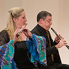 O’Connor, dressed in a flowy-armed gown, blows into her flute while Kay, wearing a dark suit, sits to her right and plays his clarinet.