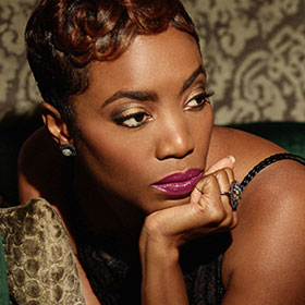 Heather Headley lounges on pillows with her hand supporting her head.