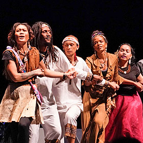 Five musicians with arms intertwined dance in a row across the stage.