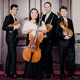 A formally dressed ensemble of three men and a woman hold their string instruments and smile.