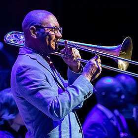 A musician is shown in profile playing a trombone.