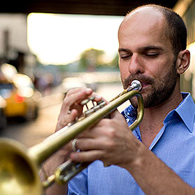A balding man looks at his trumpet while he plays.
