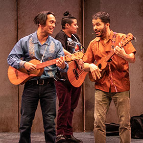 Three Latinx guitarists play and sing.